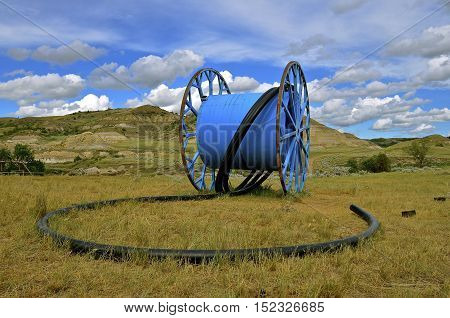 A huge metal reel for holding hose in oil country dwarfs the landscape