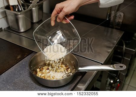 Chef is pouring rice to stewpan, commercial kitchen