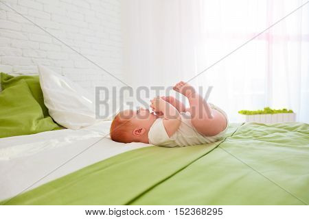 funny baby playing with legs while lying in bed at home