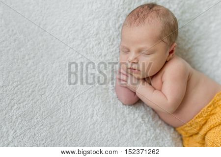 sweet sleeping newborn boy in yellow panties with head on his hand