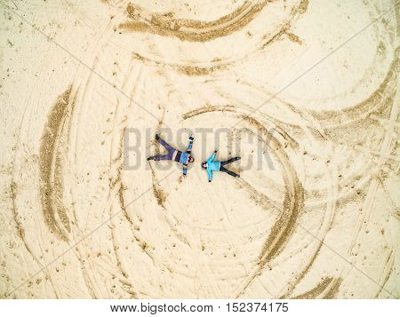 Aerial view - man and girl lie on a sandy ground, top view