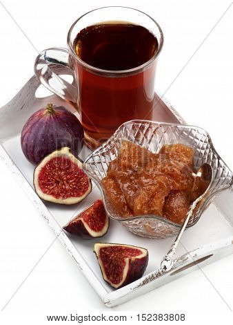 Arrangement of Delicious Homemade Fig Jam in Glass Kremanka with Fresh Fig Fruits and Glass Cup of Tea in White Wooden Tray closeup on White background