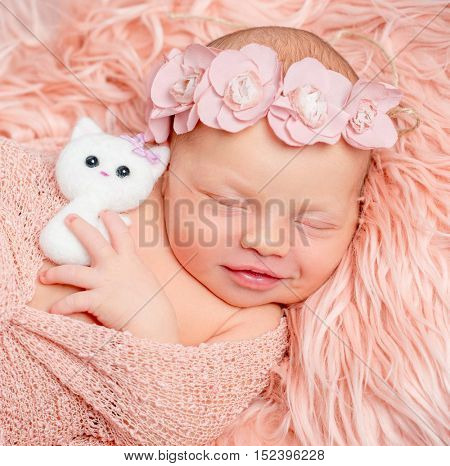 lovely sleeping newborn girl holding toy on pink fluffy blanket