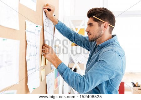 Serius casual businessman posting business plan at the office board while sitting at the desk