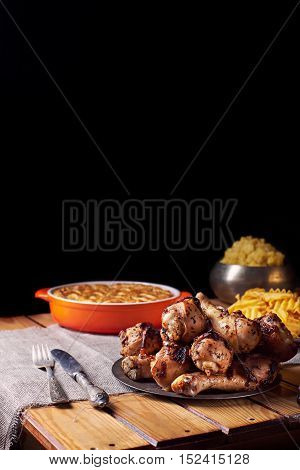 Close view of grilled chicken legs, knife, and fork mash potatoes, pumpkin pie on a table on a black background. Dark photo. Vertical shot