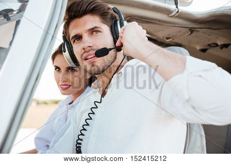 Close up portrait of a young pilot and beautiful stewardess sitting together inside airplane cabin waiting to take off