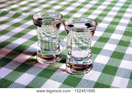 Two glasses with sambuca on the table with green-white checkered tablecloth.