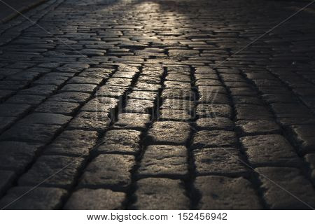 Black cobbled stone road background with reflection of light seen on the road. Black or dark grey stone pavement texture. light on the stone pavement