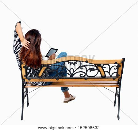 back view woman sitting on bench and looks at screen of tablet. Rear view people collection. Isolated over white background. Brunette reading e-book on park bench throwing his hands behind his head