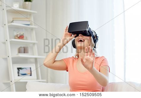 technology, virtual reality, entertainment and people concept - happy young woman in virtual reality headset or 3d glasses and headphones playing game at home and touching something invisible