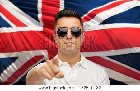 summer, accessories, style and people concept - middle aged latin man in white polo t-shirt and sunglasses pointing finger over brittish flag