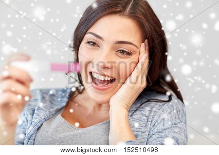 pregnancy, fertility, maternity, emotions and people concept - happy smiling woman looking at pregnancy test at home over snow