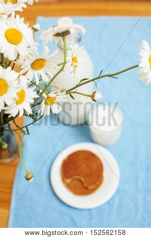 Simply stylish wooden kitchen with bottle of milk and glass on table, summer flowers camomile, healthy foog moring concept noone close up