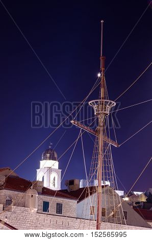 Topmast and cables of an old ship from the time of the discoveries against a clear bell tower at night.