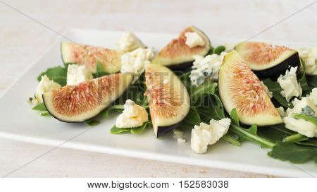 Fig arugula blue cheese salad on white plate on wooden table selective focus horizontal