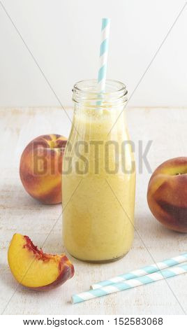 Peach fruit smoothie in glass bottle and paper straws on wooden table. Healthy lifestyle selective focus vertical