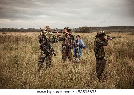 Hunting scene with hunters aiming during hunting season in rural field in overcast day with moody sky