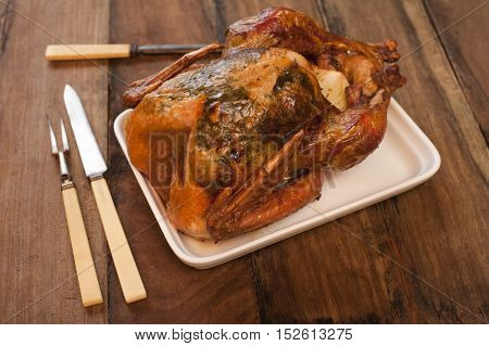 Roast chicken on a rectangular plate with a set of carving knife and fork on a wooden table waiting to be carved for dinner