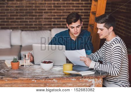 Young business owners sitting at a table at home discussing paperwork over a laptop while working together on their home based business
