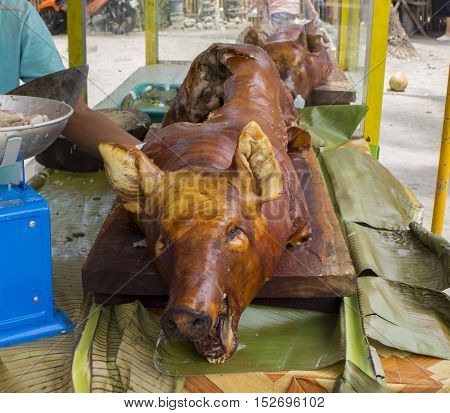 Fried whole pig on the table near a cook chief in open restaurant. Roasted meat and skin image. Barbecue pork for cutting and outdoor eating. Summer dish from meat. Spanish jamon or Philippines lechon
