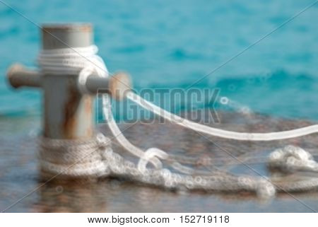 Rusty mooring bollard with ship ropes and clear turquouse sea ocen water Blurred bokeh background.