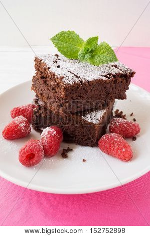 Sliced black bean brownie cake decorated with powdered sugar and mint and raspberry on on white plate selective focus vertical