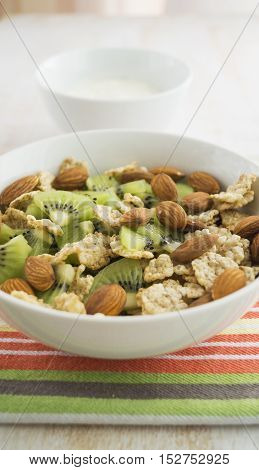 Whole grain cereal with kiwi and almond in white bowl and yogurt. Healthy breakfast. Health and diet concept selective focus close up vertical.