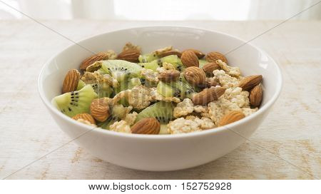 Whole grain cereal with kiwi and almond in white bowl. Healthy breakfast. Health and diet concept selective focus close up horizontal