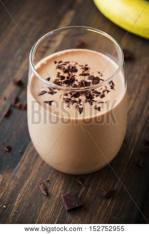 Chocolate banana smoothie in glass on wooden background selective focus vertical toned