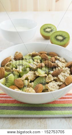 Whole grain cereal with kiwi and almond in white bowl and yogurt. Healthy breakfast. Health and diet concept selective focus close up.