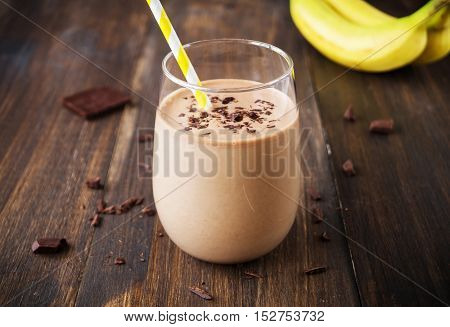 Chocolate banana smoothie in glass with paper straw on wooden background selective focus horizontal toned