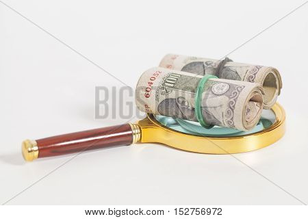 Rolls of Indian Currency Rupee Notes with magnifying glass on white background