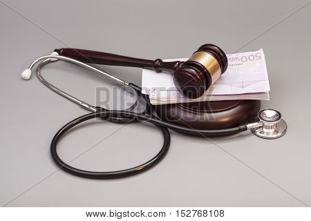 Stethoscope with judge gavel and euro banknotes on gray background