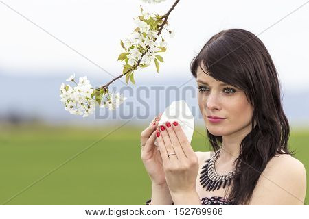 Unwell hayfever girl is pained in green spring nature season. The beautiful young woman is pained by her allergy every year. She holds a tissue in her hands.