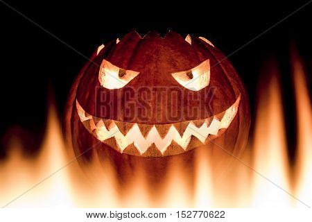 Scary carved halloween pumpkin in hot burning hell fire flames. The big helloween pumpkin has a mad face with glowing eyes and also a glow in its mouth and teeth. Perspective from bottom up.