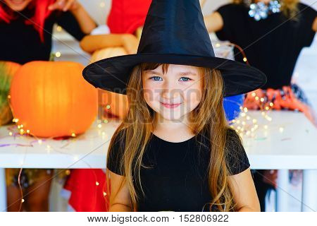Happy group of children in costumes during Halloween party playing around the table with pumpkins and bottle of potion