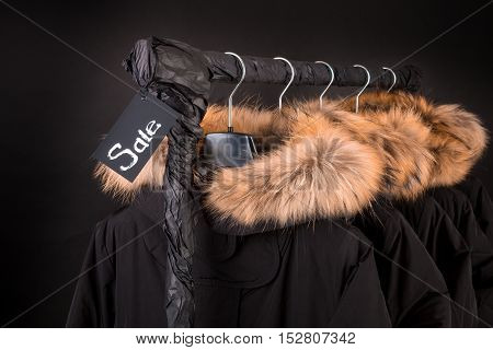 Sale Sign. A Lot Of Black Coats, Jacket With Fur On Hood Hanging  Clothes Rack.  Background.  Friday