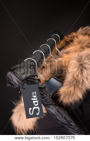 Lot Of Black Coats, Jacket With Fur On Hood Hanging  Clothes Rack.  Background. Sale Inscription.  F
