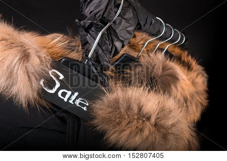 Sale Sign. A Lot Of Black Coats, Jacket With Fur On Hood Hanging  Clothes Rack.  Background.  Friday
