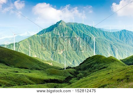 There are wind turbines that generate electricity and green mountains.