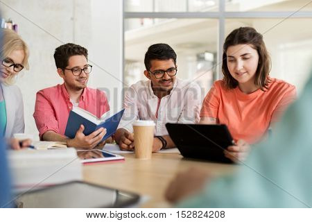 education, high school, people and technology concept - group of international students sitting at table with tablet pc computers, books and notebooks at university