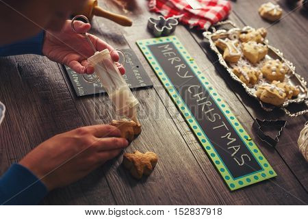 Woman decorating gingerbread cookies on woodem background