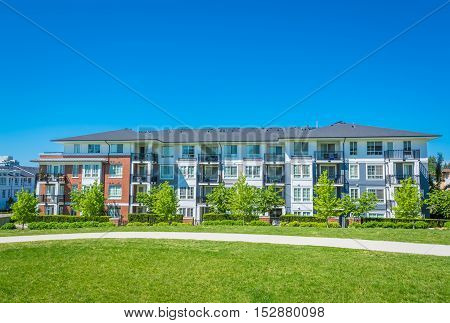Concrete pathway is crossing green lawn alongside of residential condo building. Apartment building on sunny day with blue sky background