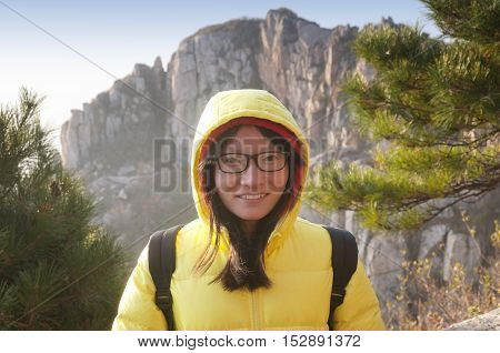 A smiling chinese woman wearing glasses and a yellow winter coat in the early morning on Taishan or Mount Tai in Shandong province China.