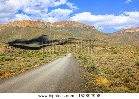 African safari in 4x4. Adventure in the African desert. Gravel mountain road in the dramatic sky, Karoo National Park in the summer, Western Cape province of South Africa.