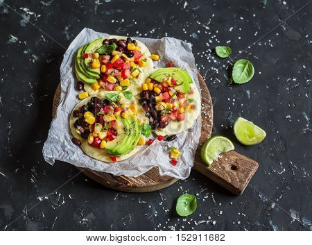 Spicy bean tostadas with corn salsa and avocado on a rustic cutting board on a dark background. Delicious vegetarian lunch or snack