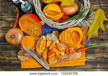Fresh ingredients for pumpkin soep with apple orange carrot and onion on wooden background
