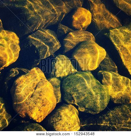 Shallow water with stones in the bottom. Aged photo. Lake Ladoga bottom with pebbles. Ripples on the surface of the stones. Vintage filter photo. Rocks through the water.