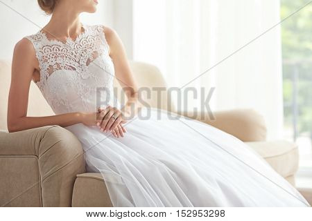 Bride in beautiful wedding gown sitting on sofa