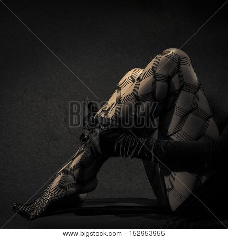 Low key special toned photo of sexy female nude legs in net tights and hands in black leather gloves against dark background
